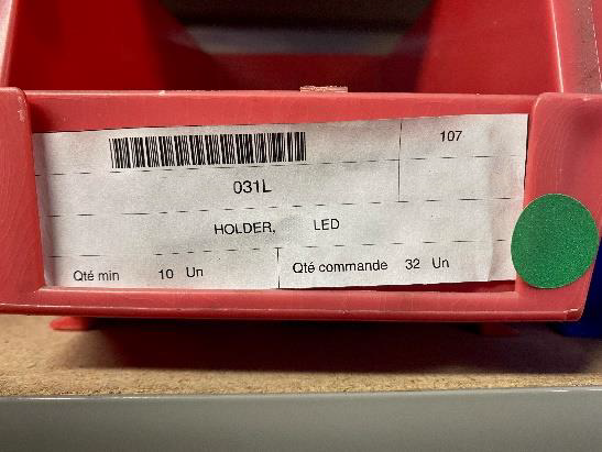 Un bac de quincaillerie rouge avec son étiquette code-barres : référence 031L, HOLDER LED, quantité minimale et quantité en commande